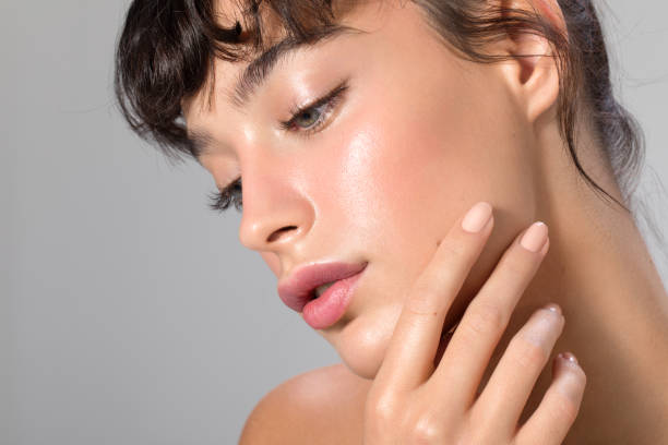 Close-up of a woman with glowing, smooth skin gently touching her cheek, exemplifying glass skin goals.